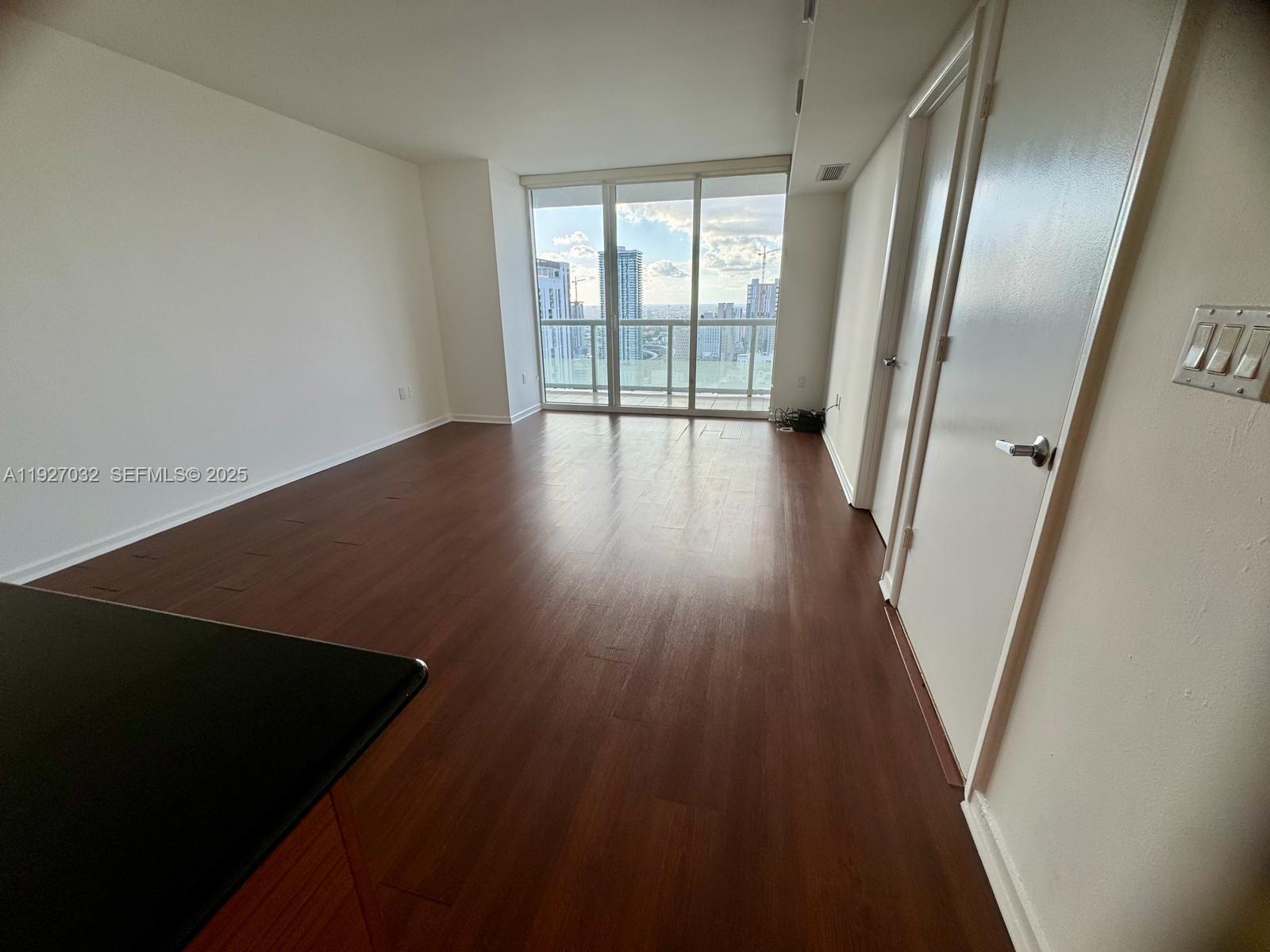 An empty living area features dark wood-look flooring, white walls, and floor-to-ceiling windows — 50 BISCAYNE Blvd # 3807, Miami FL 33132, MIAMI, FL