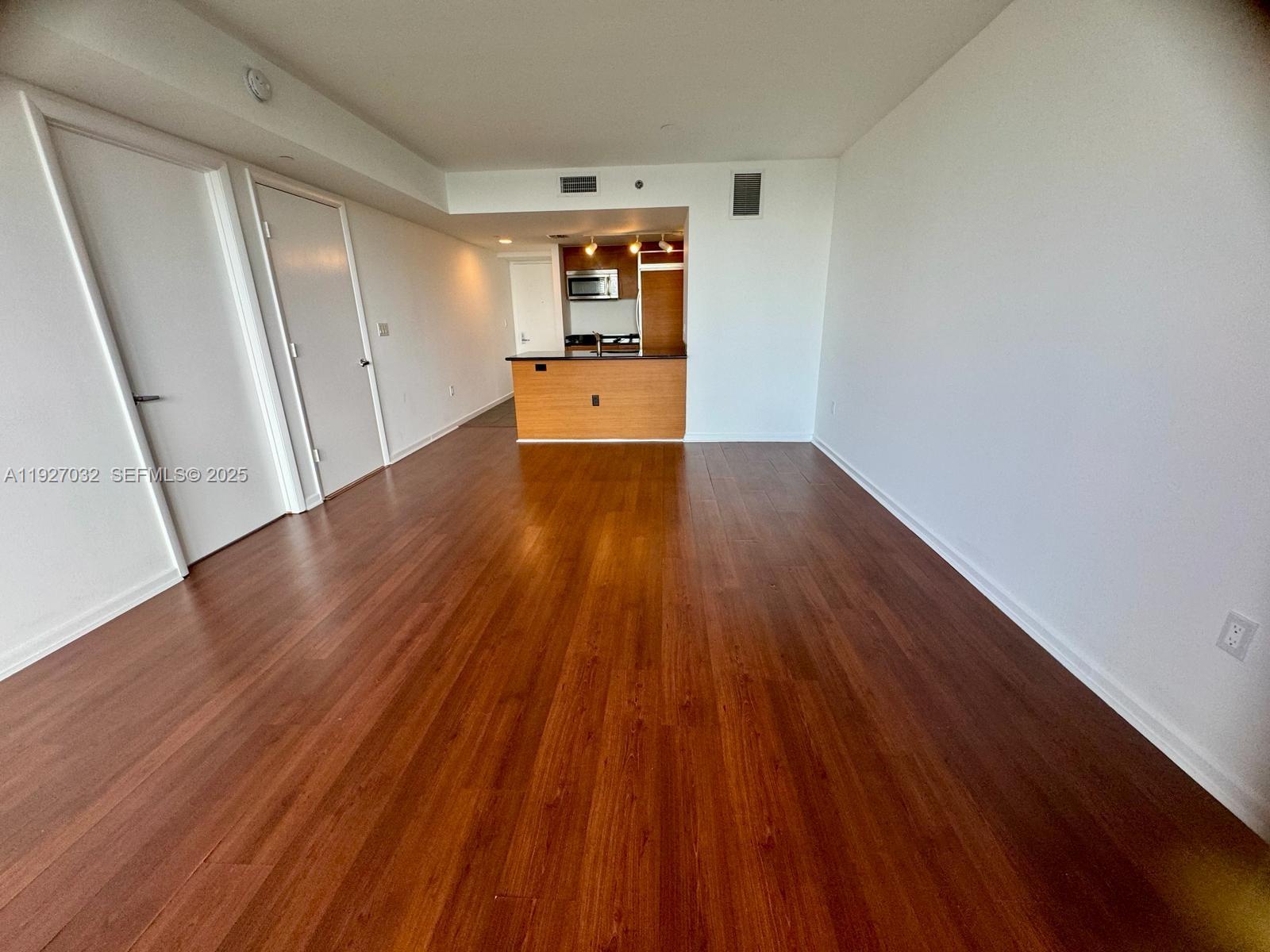 An empty living area features wood-look flooring, white walls, and an open kitchen with cabinetry — 50 BISCAYNE Blvd # 3807, Miami FL 33132, MIAMI, FL
