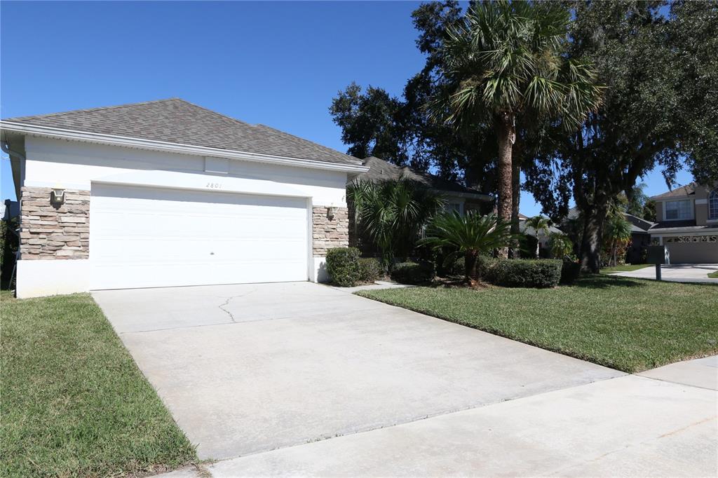 A single-story house with a white garage door, stone accents, and a concrete driveway — 2801 BAYWOOD LANE, KISSIMMEE, FL