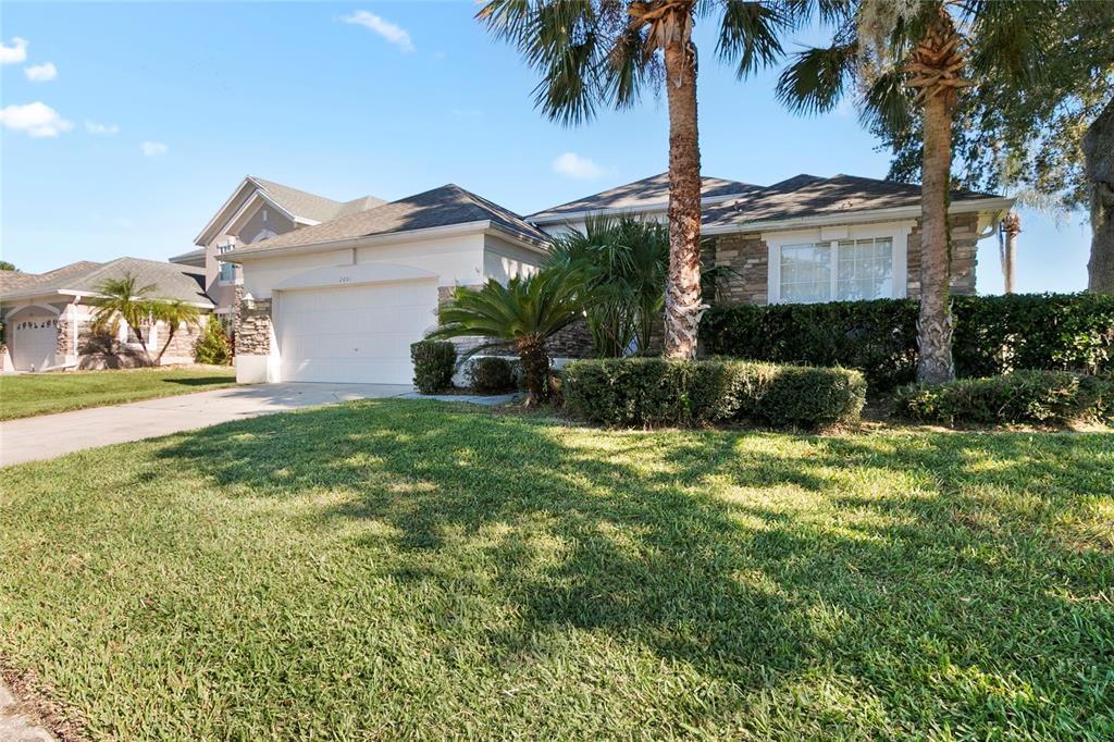 A single-story house with a white garage, stone accents, and palm trees in the front yard — 2801 BAYWOOD LANE, KISSIMMEE, FL