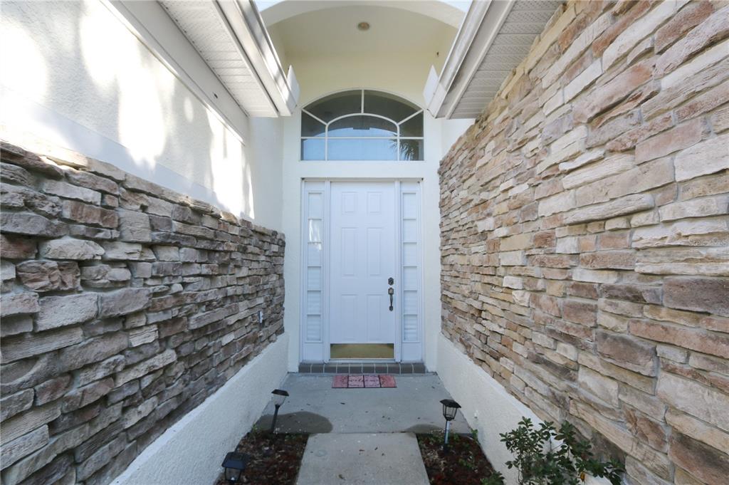 A white front door is framed by two stone veneer walls and a glass transom window — 2801 BAYWOOD LANE, KISSIMMEE, FL