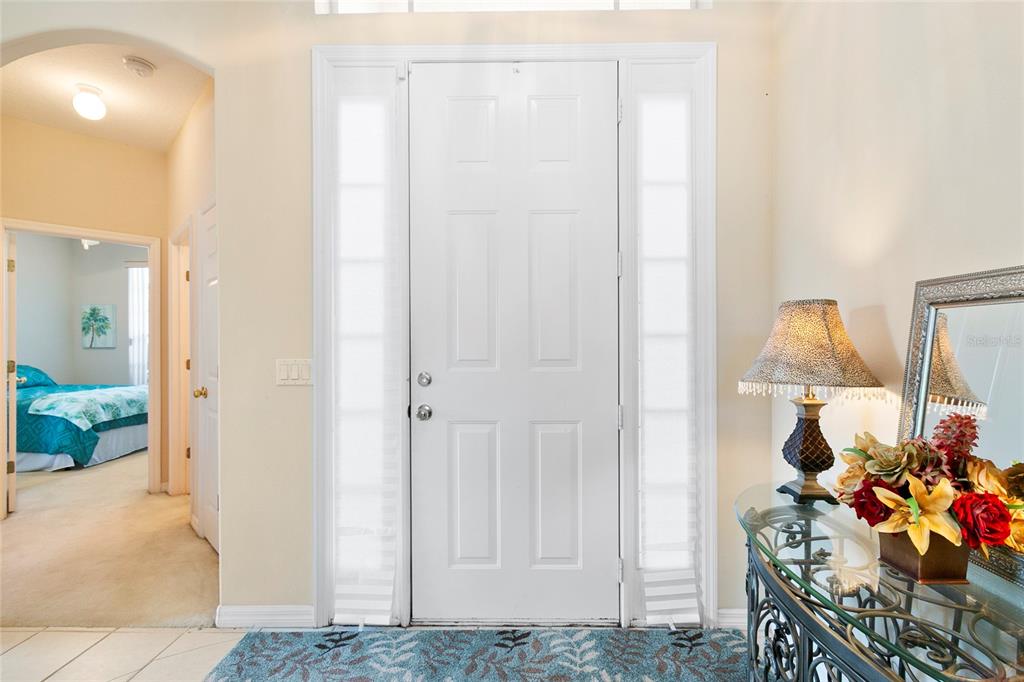 An entryway features a white front door with sidelights, a glass console table, and tile flooring — 2801 BAYWOOD LANE, KISSIMMEE, FL