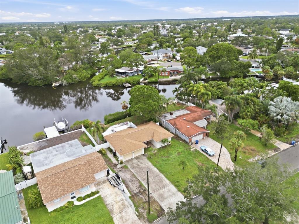 An aerial view shows three waterfront houses with driveways and lawns along a canal — 4400 HUNTINGTON STREET NE, ST PETERSBURG, FL