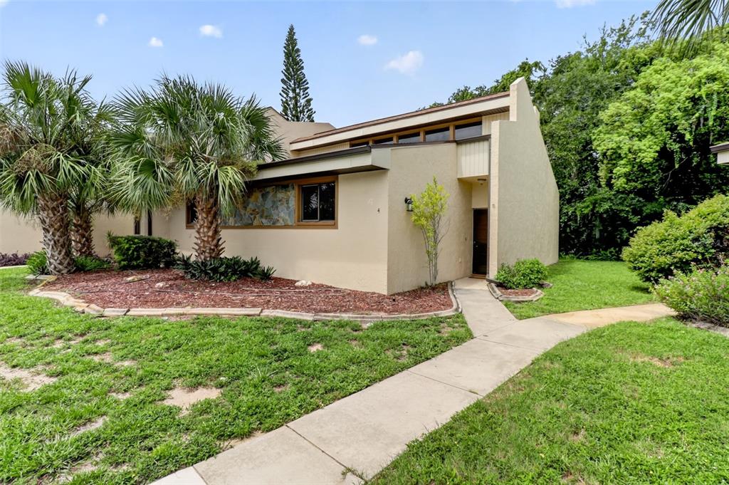 A beige exterior wall features palm trees and a landscaped garden bed with green plants — 7025 COGNAC DRIVE UNIT 4, NEW PORT RICHEY, FL