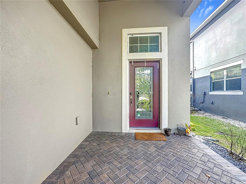 A covered entryway features a brick paver floor and a purple front door with glass — 10658 BANNAN STREET, ORLANDO, FL
