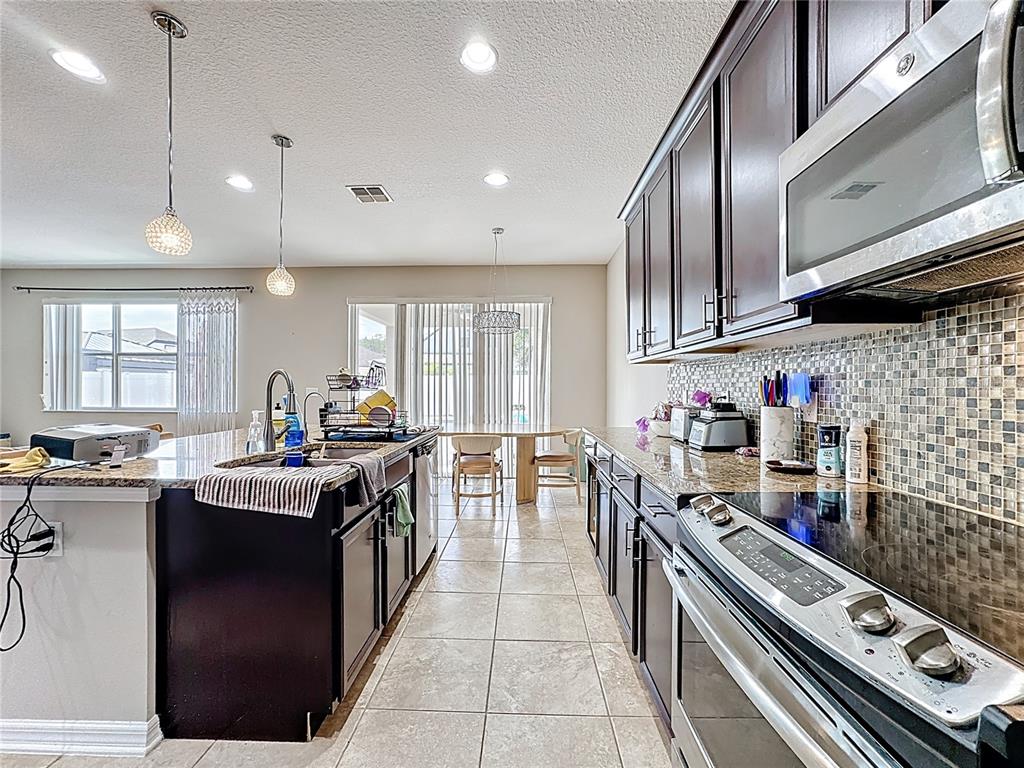 A kitchen features dark wood cabinets, granite countertops, a tile backsplash, and a center island — 10658 BANNAN STREET, ORLANDO, FL