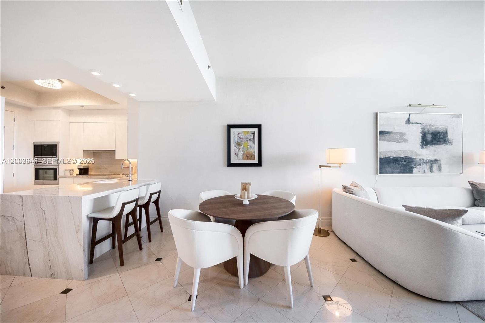 An open-concept living and dining area features a marble kitchen island and white furniture — 100 S Pointe Dr # 702, Miami Beach FL 33139, MIAMI BEACH, FL