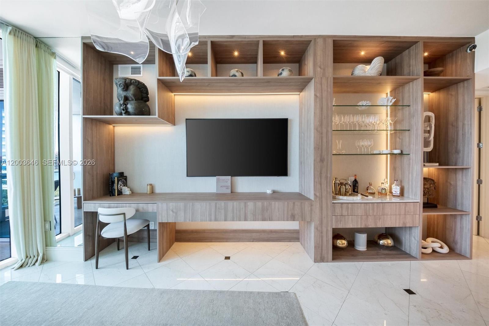 A modern living room features a built-in wood media console with integrated shelving and lighting — 100 S Pointe Dr # 702, Miami Beach FL 33139, MIAMI BEACH, FL