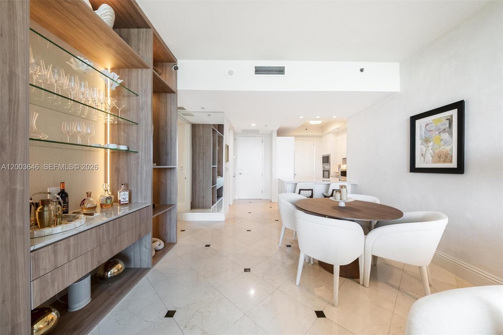 A dining area features a round wooden table, white chairs, and a built-in display cabinet — 100 S Pointe Dr # 702, Miami Beach FL 33139, MIAMI BEACH, FL