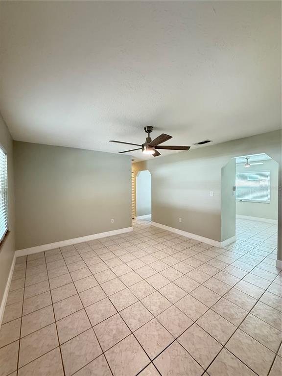An empty room with light-colored tile flooring, a ceiling fan, and arched doorways — 221 SHERRY AVE, WINTER SPRINGS, FL