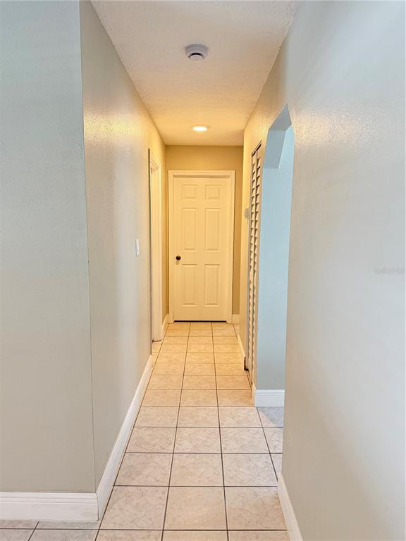 A hallway with light-colored walls, tiled flooring, and a white door at the end — 221 SHERRY AVE, WINTER SPRINGS, FL