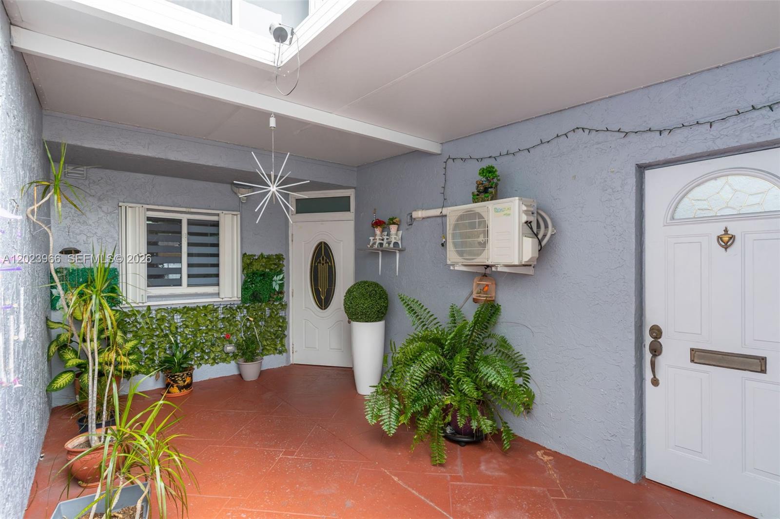 A covered outdoor patio features red tile flooring, potted plants, and two white entry doors — 3770 W 8th Ln # 27, Hialeah FL 33012, HIALEAH, FL