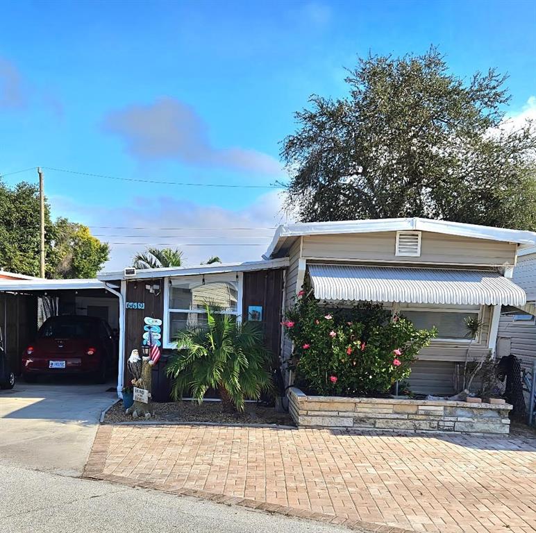 A single-story manufactured home with a brick-paved driveway, a carport, and a stone planter — 6619 NEW JERSEY STREET, BRADENTON, FL