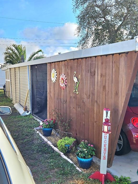 A wooden privacy fence borders a carport with potted plants and a decorative sign — 6619 NEW JERSEY STREET, BRADENTON, FL