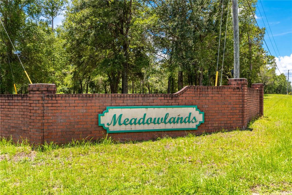 A brick wall with a sign reading Meadowlands stands in front of a wooded area — Lot 5 SW MEADOWLANDS DRIVE, LAKE CITY, FL