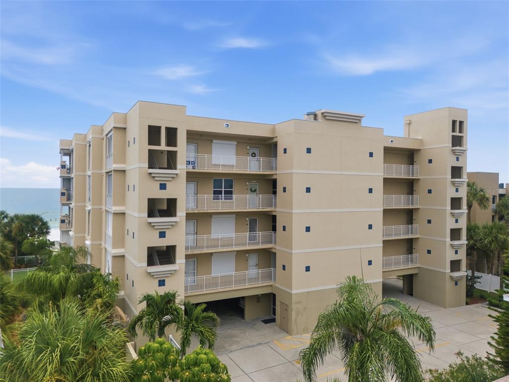 An exterior view of a multi-story tan apartment building with balconies and a ground-level parking area — 2 15TH AVENUE UNIT 303, INDIAN ROCKS BEACH, FL