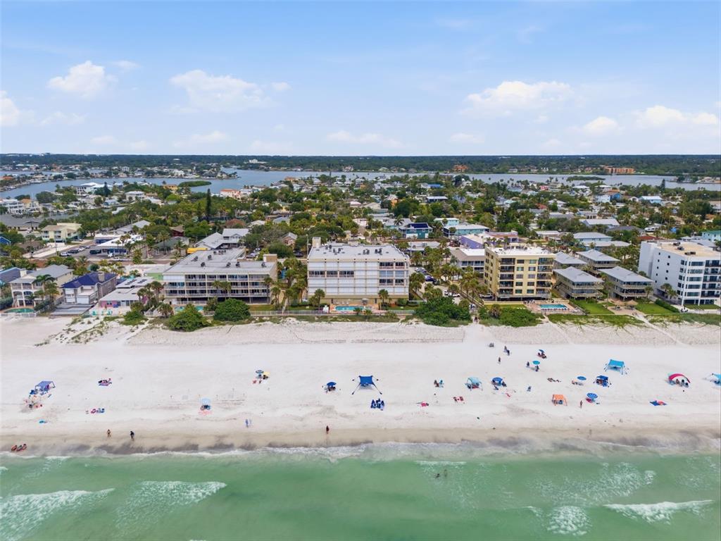 An aerial view shows a sandy beach with beachgoers in front of several waterfront apartment buildings — 2 15TH AVENUE UNIT 303, INDIAN ROCKS BEACH, FL