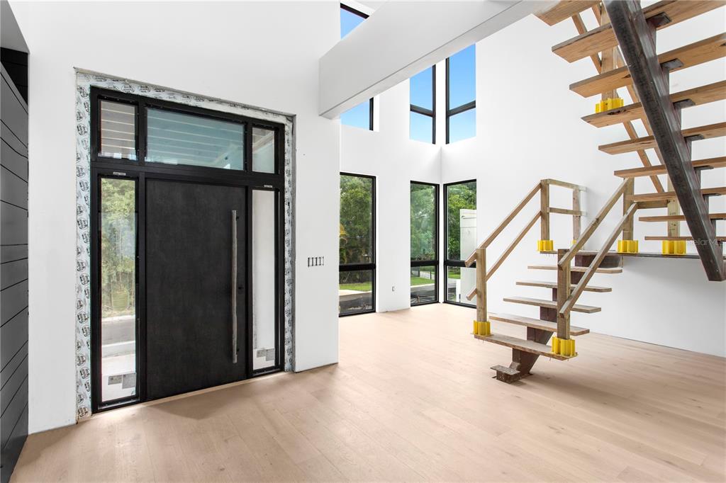 An entryway with light wood floors, a modern black door, and an unfinished wooden staircase — 2309 N RIVERSIDE DRIVE, TAMPA, FL
