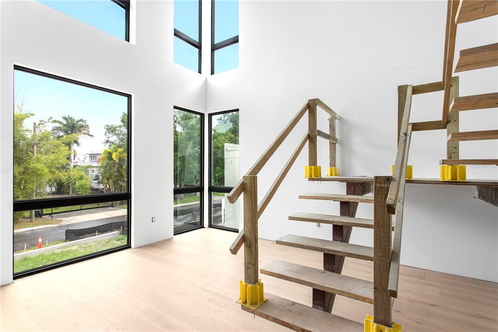 A modern room with light wood floors, large windows, and an unfinished wooden staircase — 2309 N RIVERSIDE DRIVE, TAMPA, FL