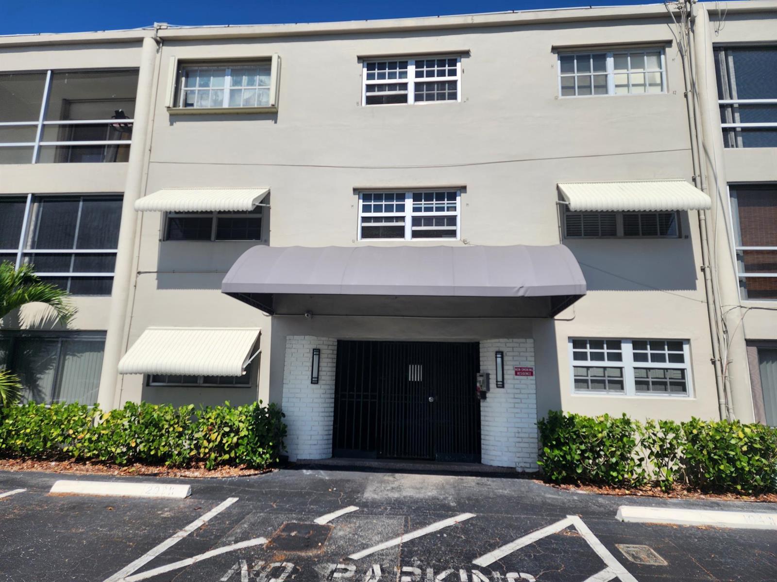 The exterior of a multi-story apartment building features a central entrance with a gray awning — 2301 NE 14th St Causeway # 305e, Pompano Beach FL 33062, POMPANO BEACH, FL