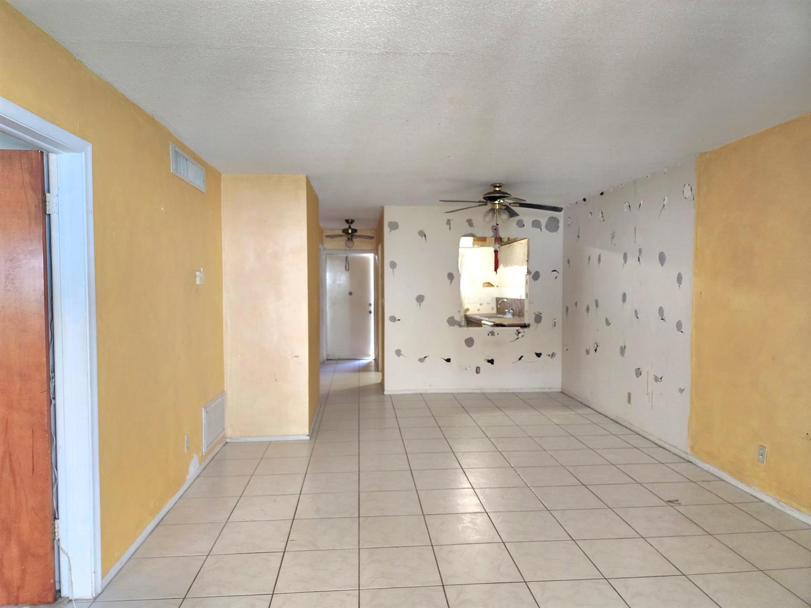 An empty room with yellow and white walls, tiled flooring, and a kitchen pass-through window — 2301 NE 14th St Causeway # 305e, Pompano Beach FL 33062, POMPANO BEACH, FL