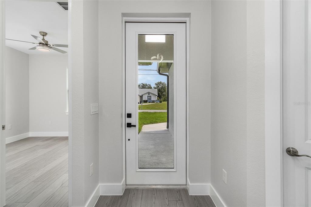 A white door with a glass panel opens to a view of a neighborhood street — 26221 SANDHILL BOULEVARD, PUNTA GORDA, FL