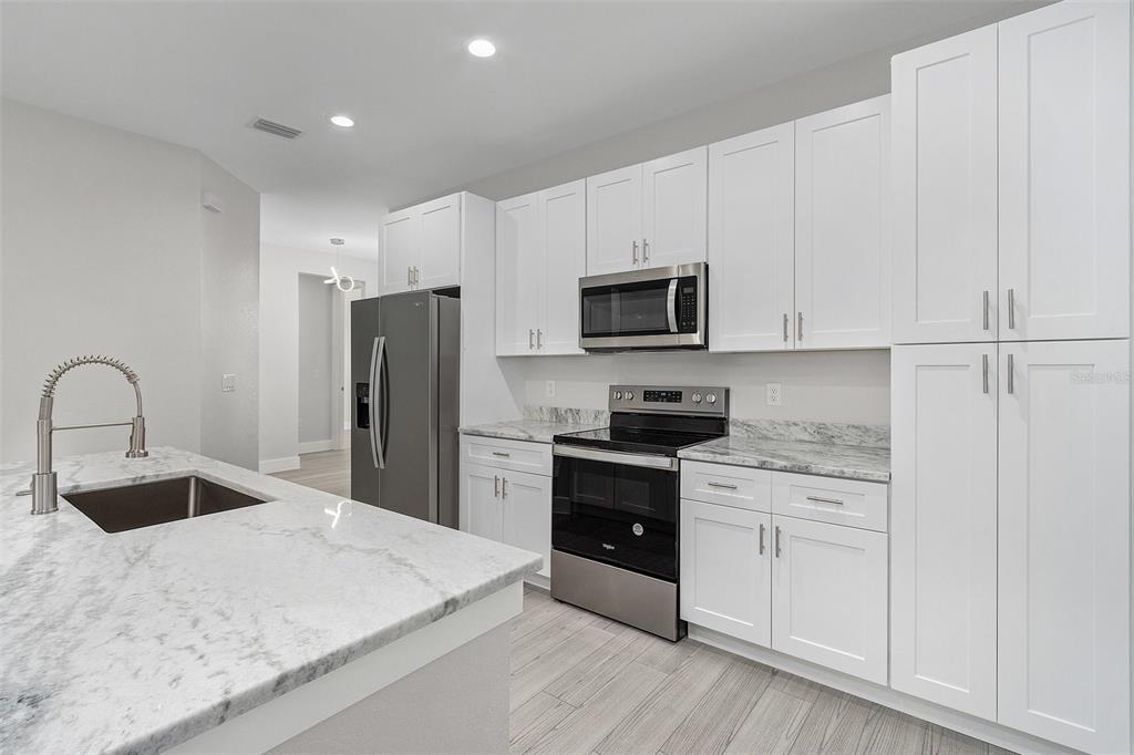 A modern kitchen features white cabinets, stainless steel appliances, and a marble-patterned island countertop — 26221 SANDHILL BOULEVARD, PUNTA GORDA, FL
