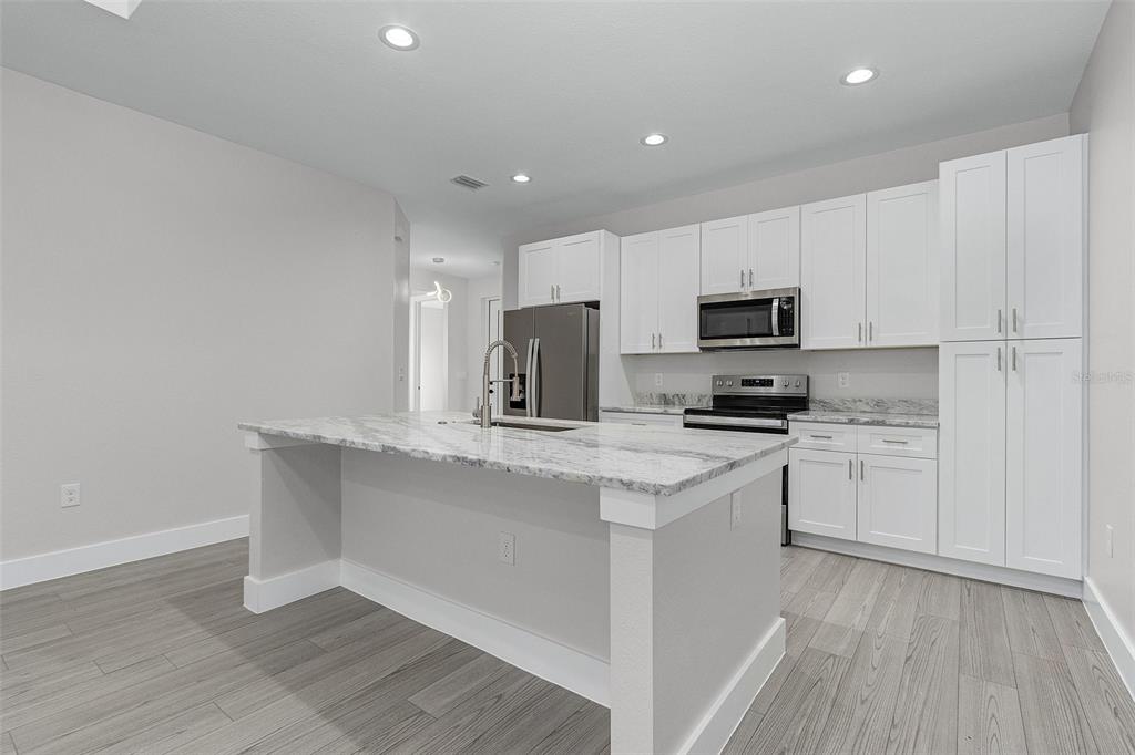 A modern kitchen features white cabinetry, a marble-topped island, and light gray wood-look flooring — 26221 SANDHILL BOULEVARD, PUNTA GORDA, FL
