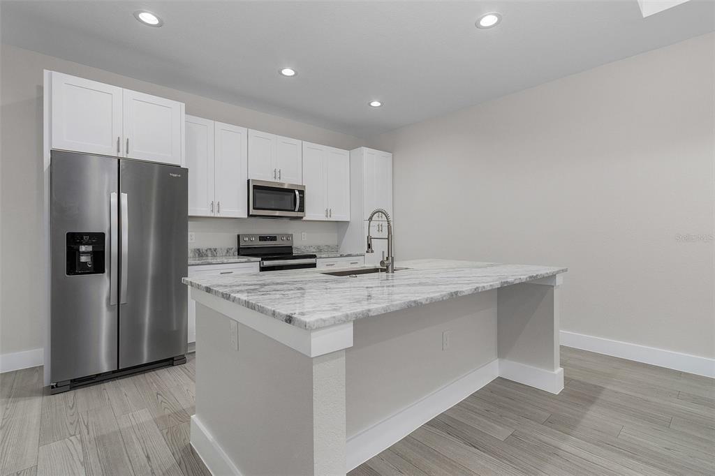 A modern kitchen features white cabinets, stainless steel appliances, and a marble-topped island — 26221 SANDHILL BOULEVARD, PUNTA GORDA, FL