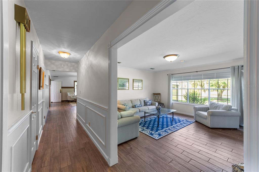 A hallway with wood-look tile flooring leads into a living room with striped furniture — 5310 NW 78TH COURT, OCALA, FL