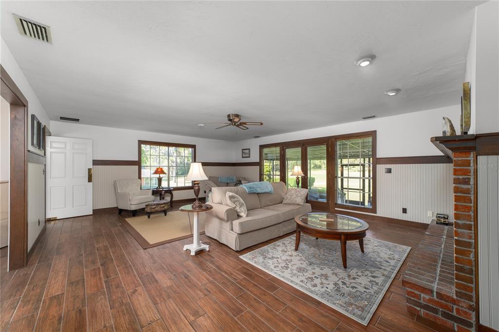 A living room features wood-look tile floors, wainscoting, a brick fireplace, and a beige sofa — 5310 NW 78TH COURT, OCALA, FL
