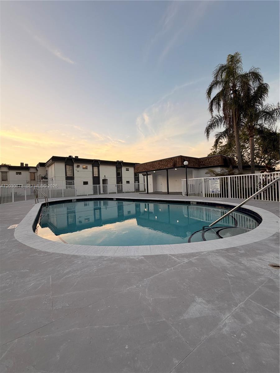 A swimming pool with a concrete deck is surrounded by a white fence and buildings — 7250 SW 94th Pl # B8, Miami FL 33173, MIAMI, FL
