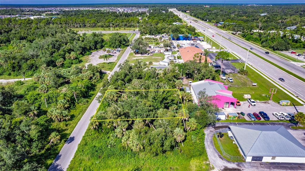 An aerial view shows a wooded lot outlined in yellow next to commercial buildings — 1104 BUENA VISTA CIRCLE, PORT CHARLOTTE, FL