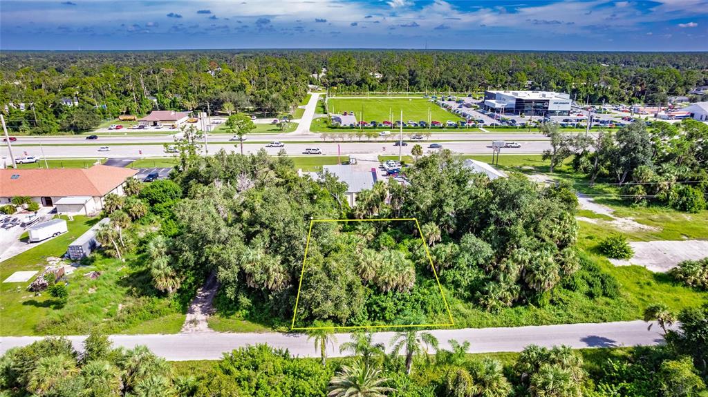An aerial view shows a rectangular, tree-covered vacant lot outlined in yellow near a road — 1104 BUENA VISTA CIRCLE, PORT CHARLOTTE, FL