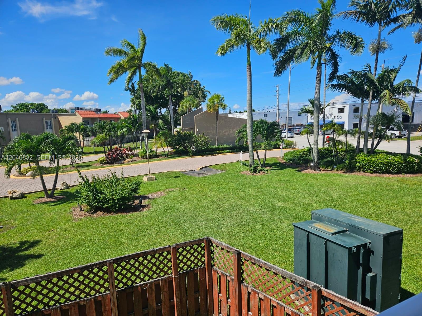 A view from a balcony overlooking a grassy lawn, palm trees, and a parking area — 4900 NW 79th Ave # 206, Doral FL 33166, DORAL, FL