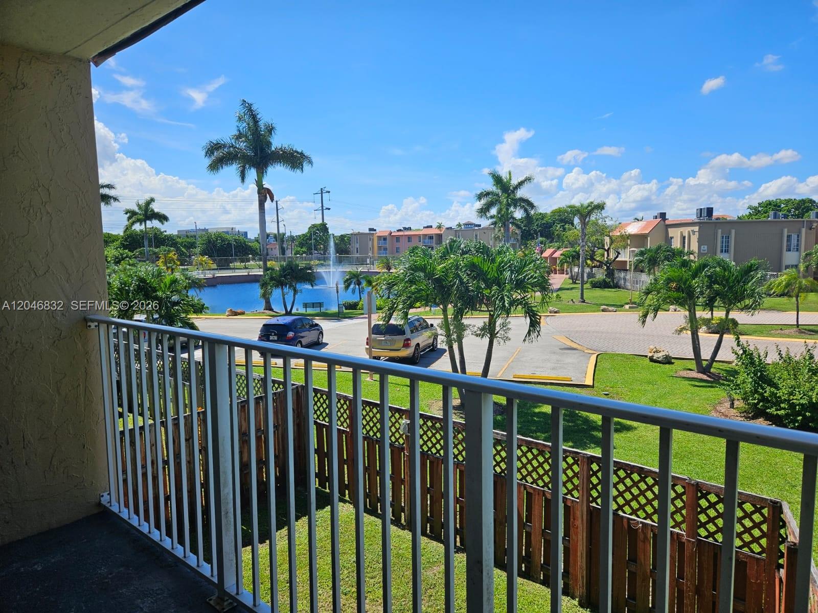 A balcony view overlooks a parking lot, a small pond with a fountain, and palm trees — 4900 NW 79th Ave # 206, Doral FL 33166, DORAL, FL