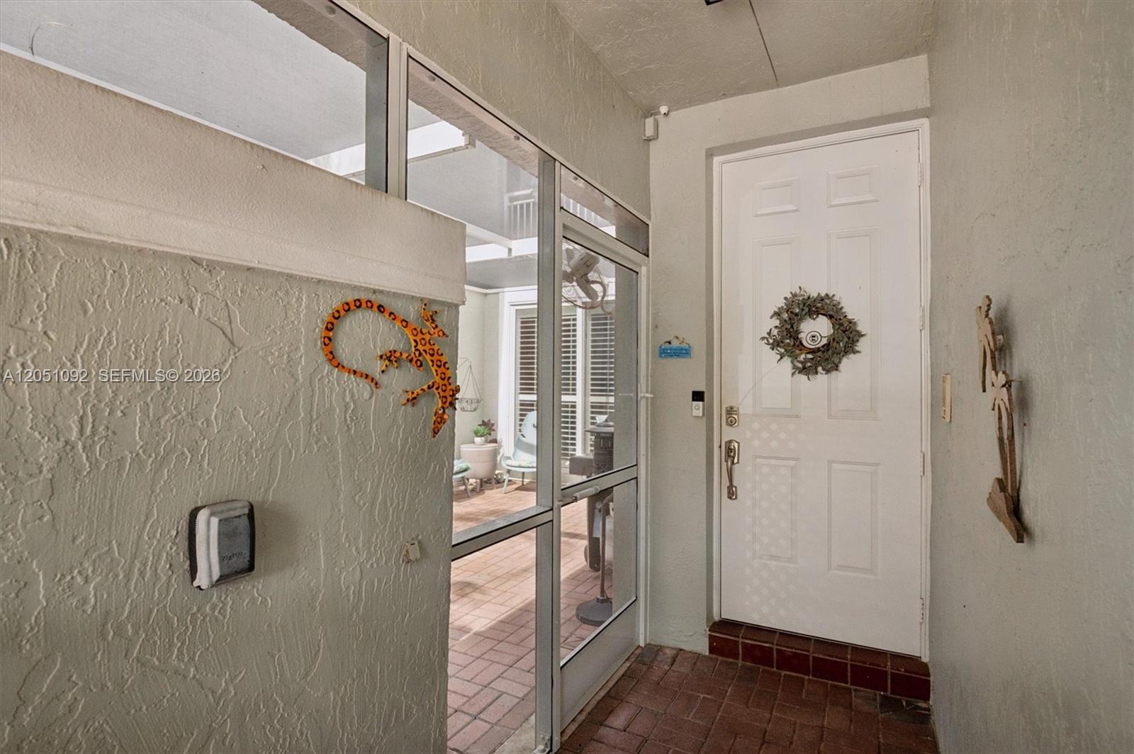 A covered entryway features a white door, a brick floor, and decorative wall art — 1140 Weeping Willow Way, Hollywood FL 33019, HOLLYWOOD, FL