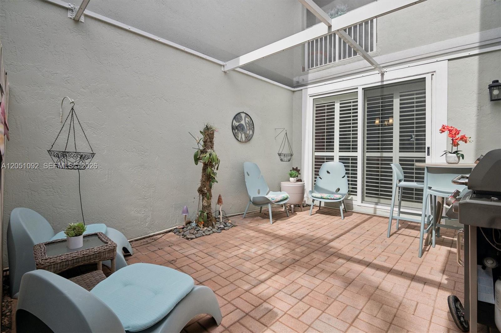 A screened-in patio features light blue chairs, a brick floor, and a small tree — 1140 Weeping Willow Way, Hollywood FL 33019, HOLLYWOOD, FL