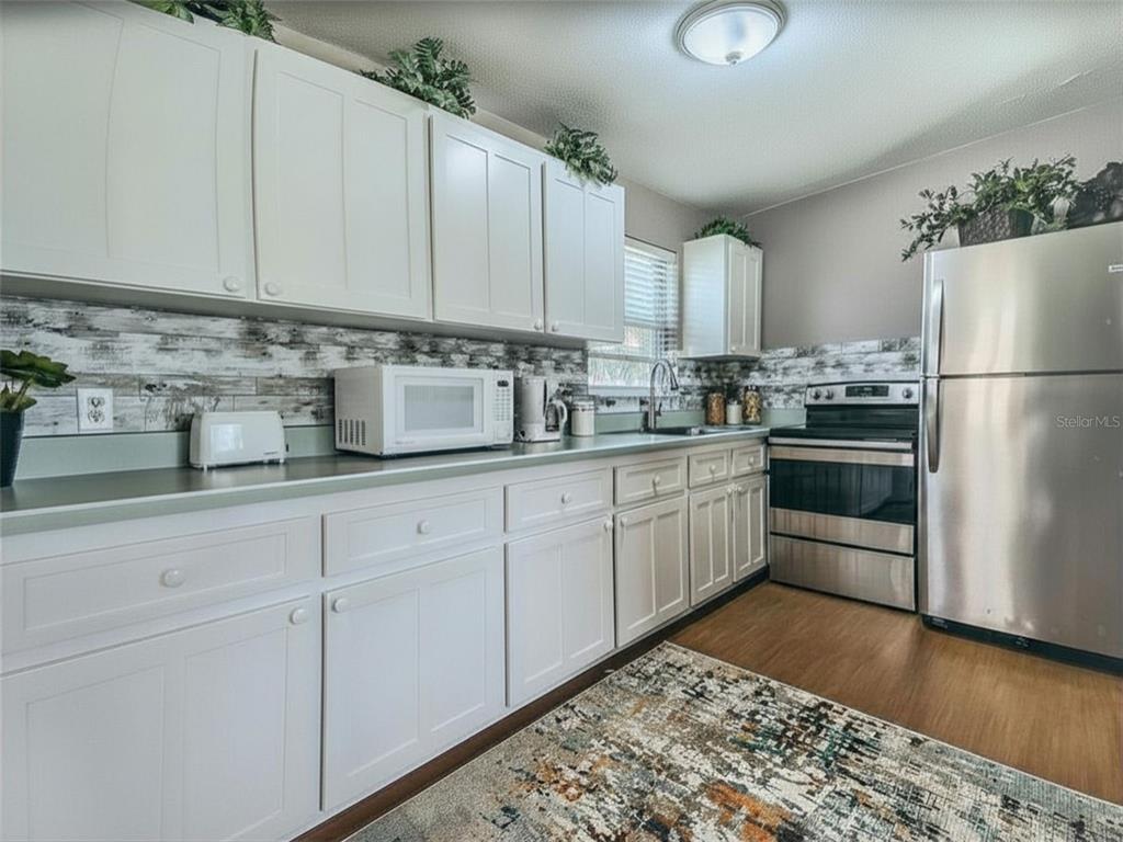 A kitchen features white cabinets, stainless steel appliances, and a wood-look backsplash — 3114 ESPERANZA AVENUE, DAYTONA BEACH SHORES, FL