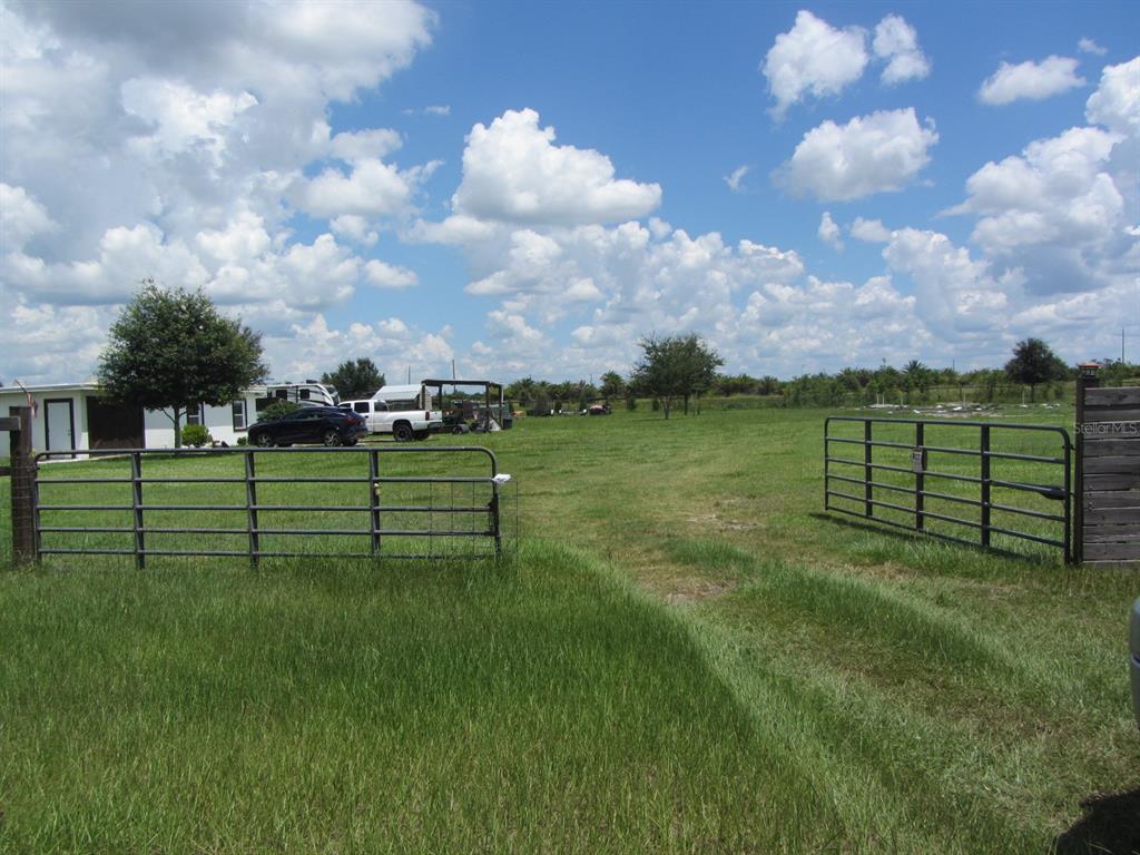 A metal gate opens to a large, grassy field with a house and vehicles nearby — 46365 STATE ROAD 64 E, MYAKKA CITY, FL