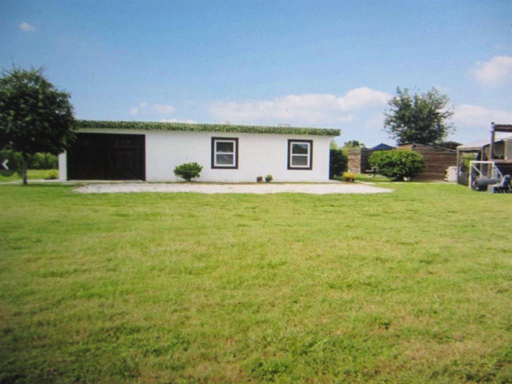 A white, single-story building with a garage and two windows sits on a grassy lot — 46365 STATE ROAD 64 E, MYAKKA CITY, FL