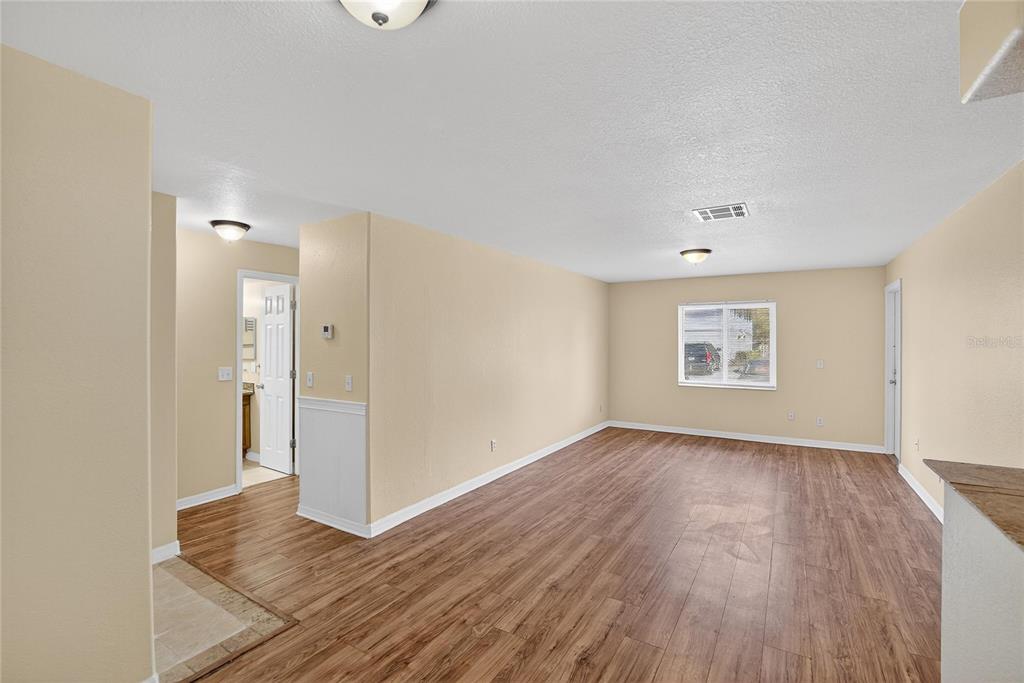 An empty living area features light-colored walls, wood-look flooring, and a window overlooking a driveway — 202 RED MAPLE PLACE UNIT 202, BRANDON, FL