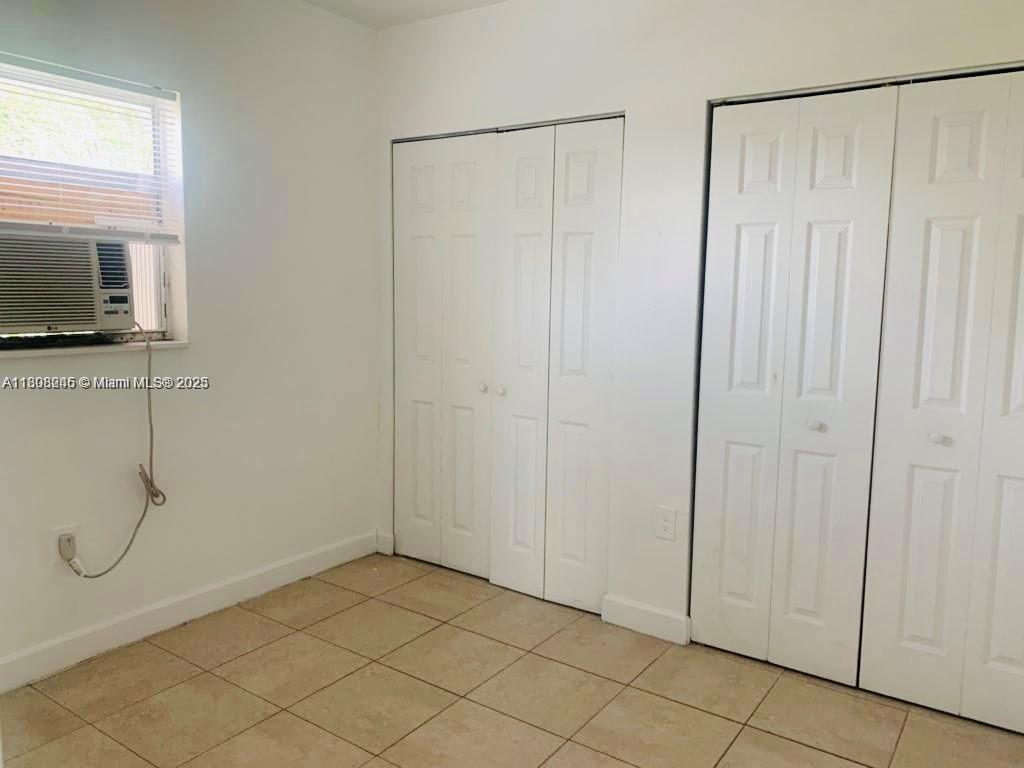 A bedroom features white walls, tiled flooring, two sets of closet doors, and a window unit — 401 N DIXIE HWY # 6, Hallandale Beach FL 33009, HALLANDALE BEACH, FL