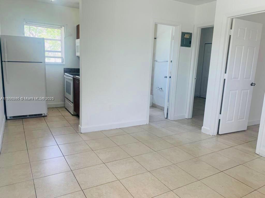 A kitchen with a white refrigerator and tiled floors opens into a hallway — 401 N DIXIE HWY # 6, Hallandale Beach FL 33009, HALLANDALE BEACH, FL