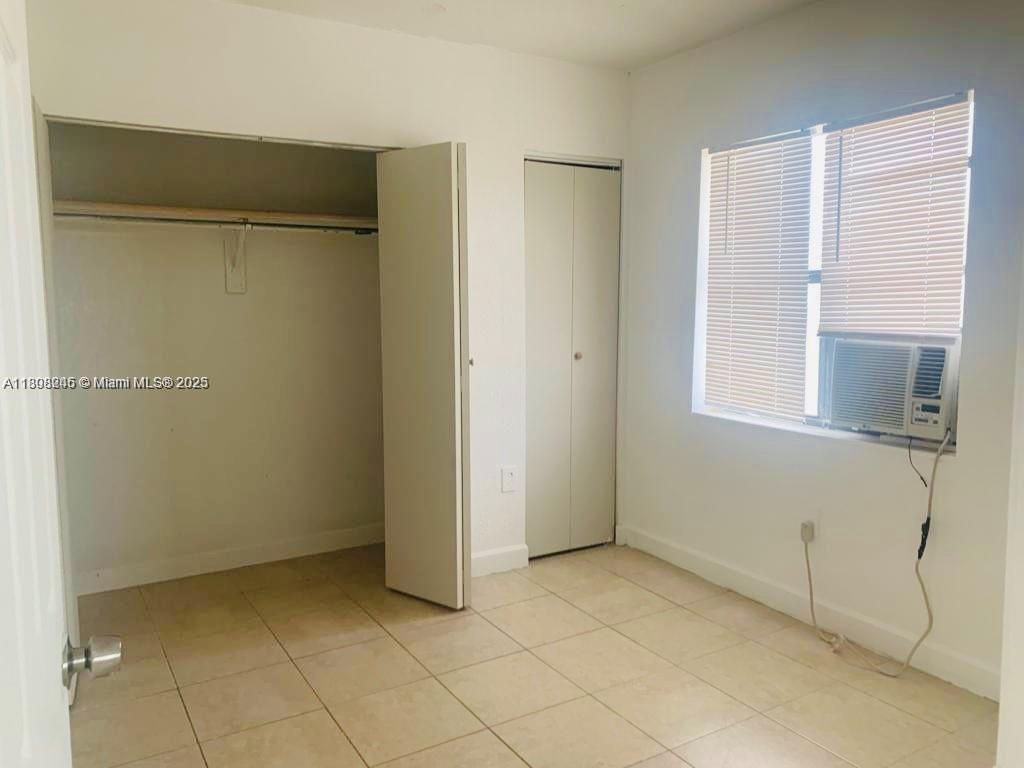 This bedroom features white walls, tiled flooring, two closets, and a window with an air conditioner — 401 N DIXIE HWY # 6, Hallandale Beach FL 33009, HALLANDALE BEACH, FL