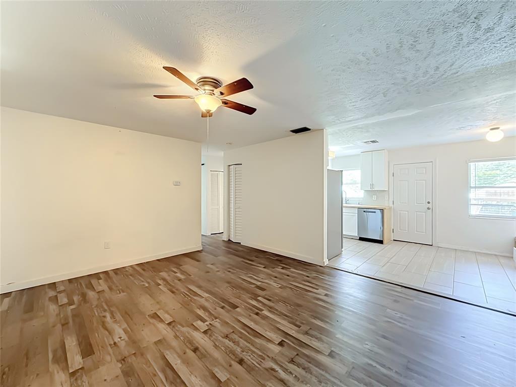 A living room with wood-look flooring transitions into a tiled kitchen area with white cabinets — 1405 PEMBROOK DRIVE, LEESBURG, FL
