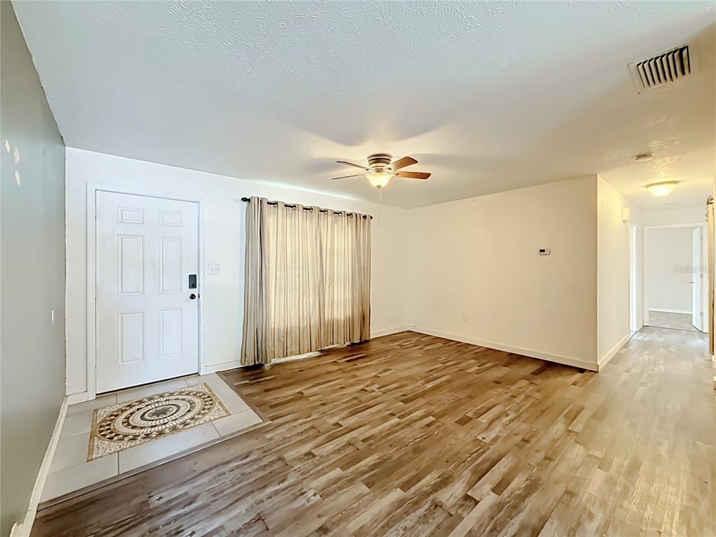 A living room features wood-look flooring, a ceiling fan, a front door, and beige curtains — 1405 PEMBROOK DRIVE, LEESBURG, FL
