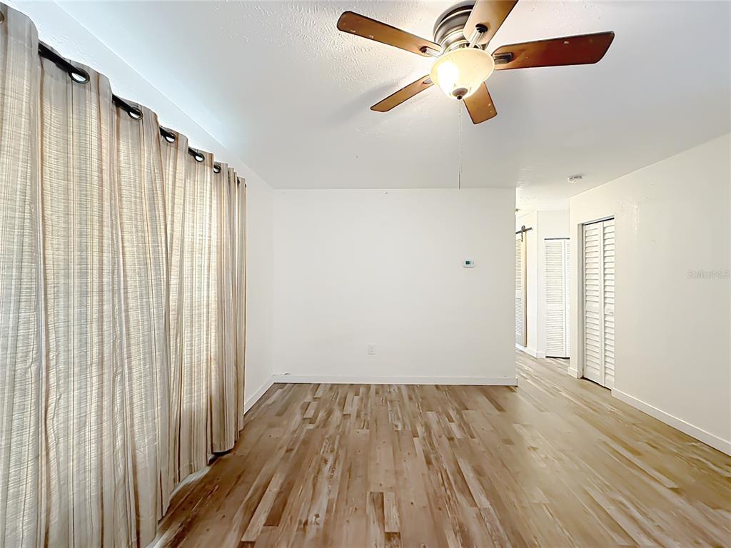 An empty room features light wood-look flooring, white walls, a ceiling fan, and floor-length curtains — 1405 PEMBROOK DRIVE, LEESBURG, FL