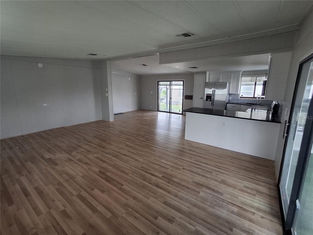 An open-concept living area features wood-look flooring, a kitchen with a peninsula, and sliding doors — 141 RAROTONGA ROAD, NORTH PORT, FL