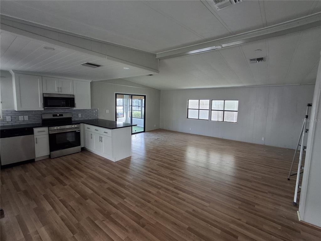 An open-concept kitchen and living area with white cabinets, stainless appliances, and wood-look flooring — 141 RAROTONGA ROAD, NORTH PORT, FL